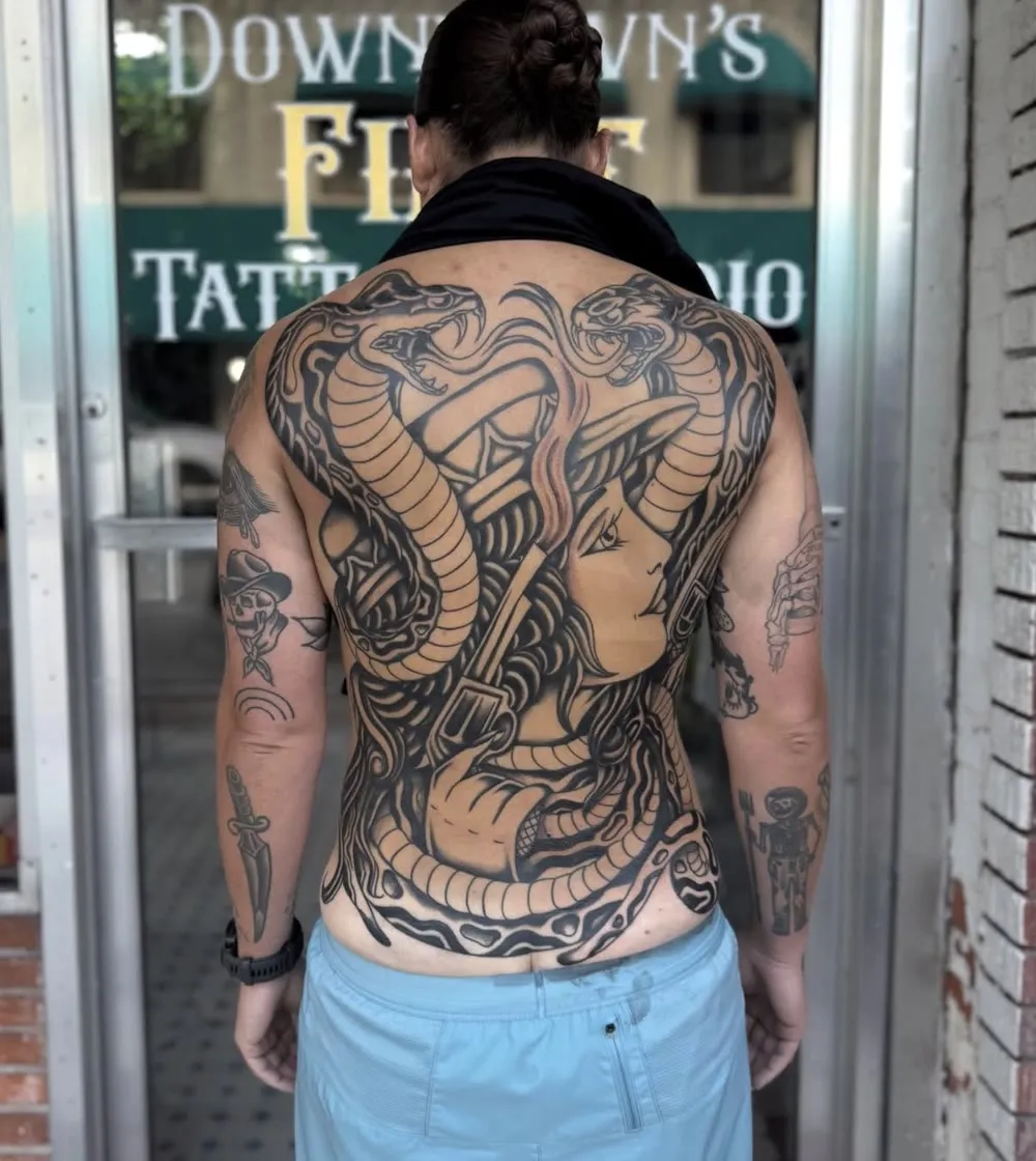 Full back piece: two cobras around a cowgirl with a revolver, black and grey traditional